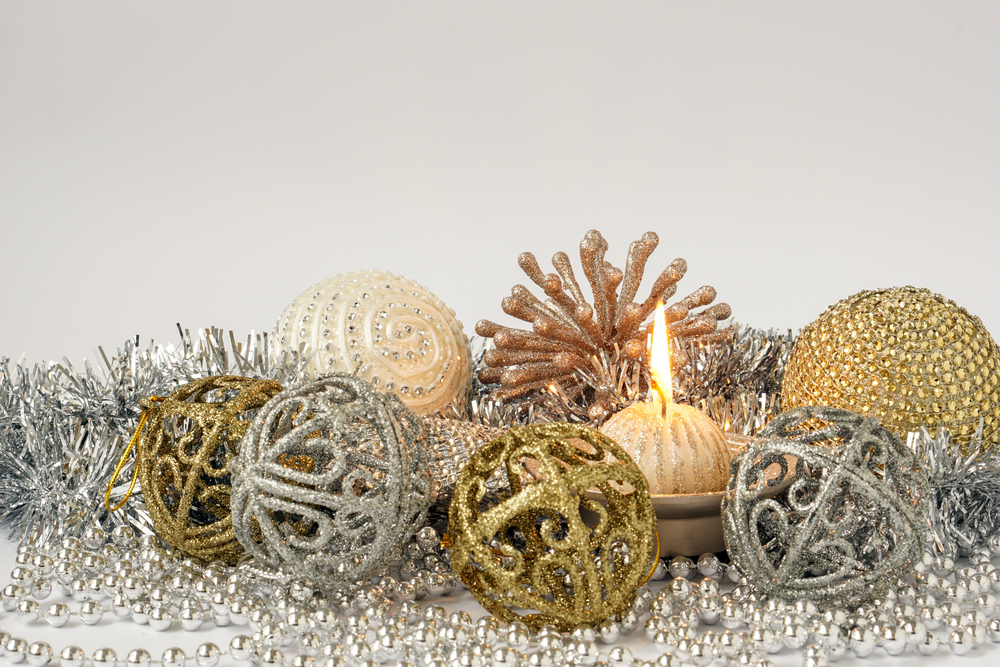 Adornos navideños en tonos dorados y plateados con una vela encendida, cuentas y guirnaldas metálicas. Esta decoración refleja las tendencias de 2024, combinando elegancia y brillo para un ambiente navideño sofisticado y festivo.